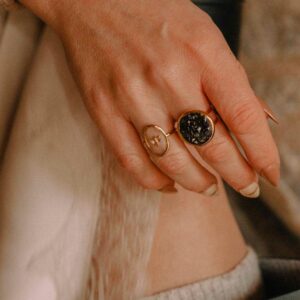 Bagues artisanales Atelier R portées à la main, modèle résine noire et modèle motif floral doré.