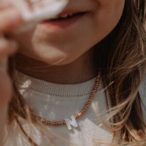 Close-up of a young girl's lower face, smiling softly, with a bead necklace and light sweater visible.