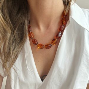 Close-up of a woman wearing an orange beaded necklace over a white blouse, focusing on the neck area.