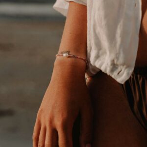 Close-up of a forearm wearing a beaded bracelet with a central pearl, along with a white short-sleeve shirt. (Informative)