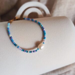 Bracelet Cassis composé de perles de rocaille bleues, lilas et blanches avec une perle d'eau douce centrale.