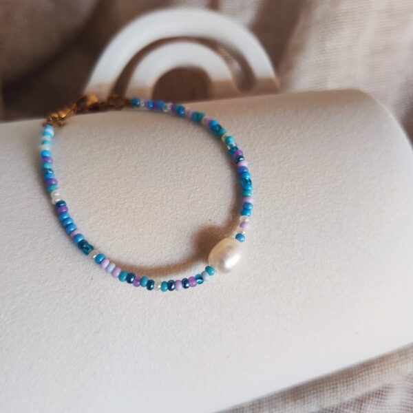 Bracelet Cassis composé de perles de rocaille bleues, lilas et blanches avec une perle d'eau douce centrale.