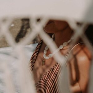 Person wearing a red-and-white striped dress with a white bead necklace, seen through sheer fabric in the foreground (blurry).