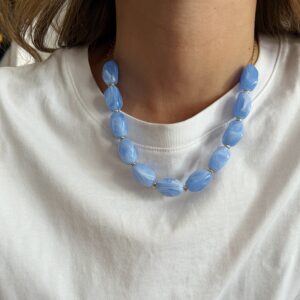 Close-up of a blue bead necklace resting on a white shirt around the neck.
