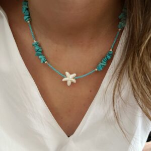 Turquoise bead necklace with a white starfish charm resting on a white V-neck blouse.