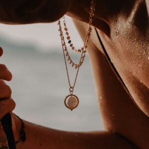 Close-up of a person wearing layered gold chains, with a circular pendant resting on the sunlit neck.