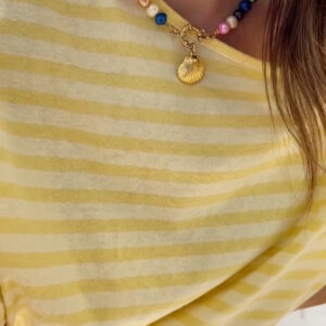Close-up of a colorful beaded necklace with a gold seashell pendant worn over a yellow striped shirt.