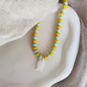 Beaded necklace with alternating yellow and mint-green beads and a white fish pendant on a display bust.